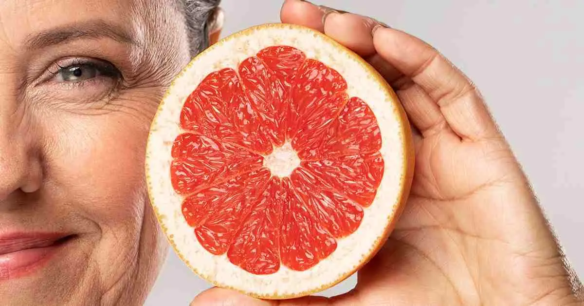 Mujer mayor sonriendo mientras sostiene medio pomelo, símbolo de los beneficios antioxidantes naturales para combatir el envejecimiento celular. 
