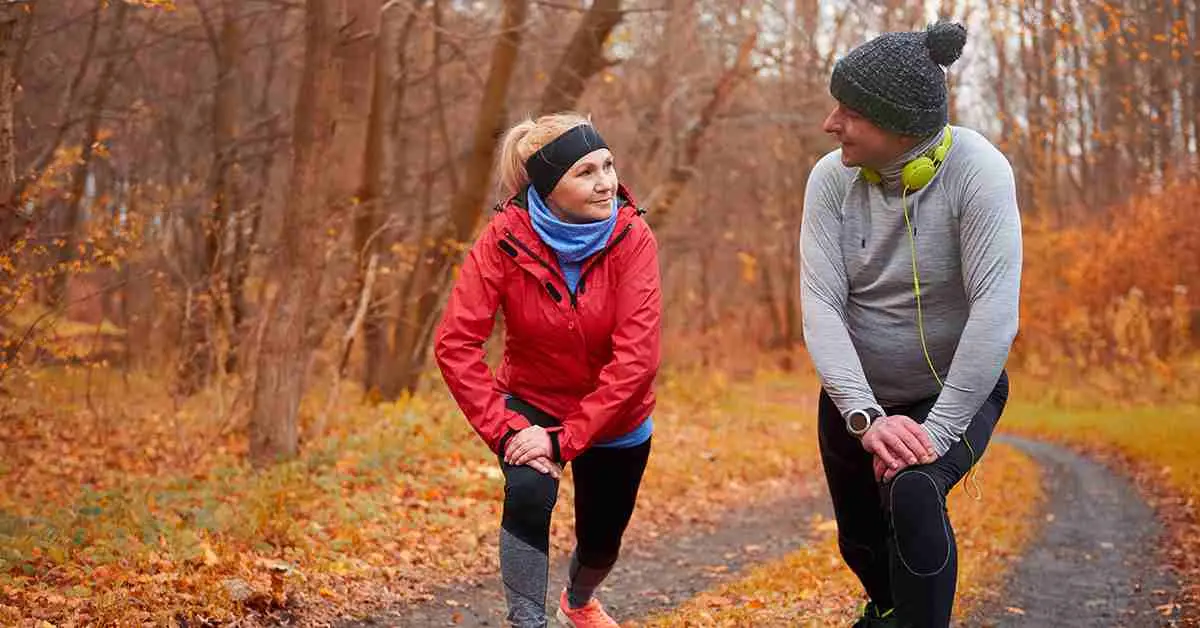 Pareja haciendo estiramientos al aire libre en otoño antes de correr, ejemplo de ejercicios para fortalecer articulaciones.