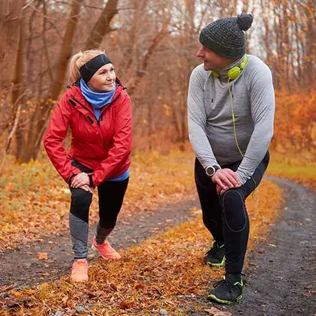 Pareja haciendo estiramientos al aire libre en otoño antes de correr, ejemplo de ejercicios para fortalecer articulaciones.