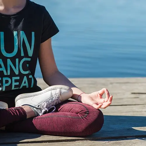 Mujer practicando meditación al aire libre junto a un lago como técnica de relajación para reducir el estrés en verano.