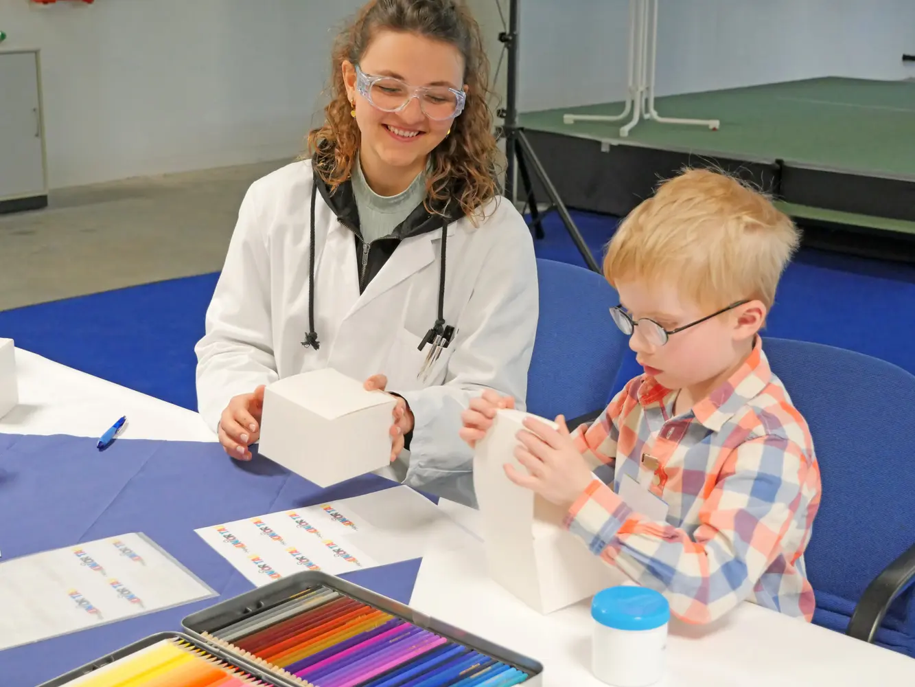 Heel-Auszubildende basteln mit den Kindern Verpackungen für ihre selbst hergestellten Gummibärchen. 