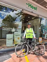 Heel Kolumbien Mitarbeiterin steht mit ihrem Fahrrad vor Heel-Apotheke.