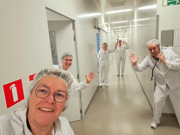 Heel Mitarbeiter aus dem Labor stehen im Flur und winken in die Kamera