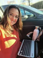 Heel Außendienstmitarbeiterin sitzt mit dem Laptop im Auto.