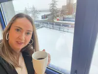 Heel Mitarbeiterin trinkt eine Tasse Kaffee, während es draußen schneit. 