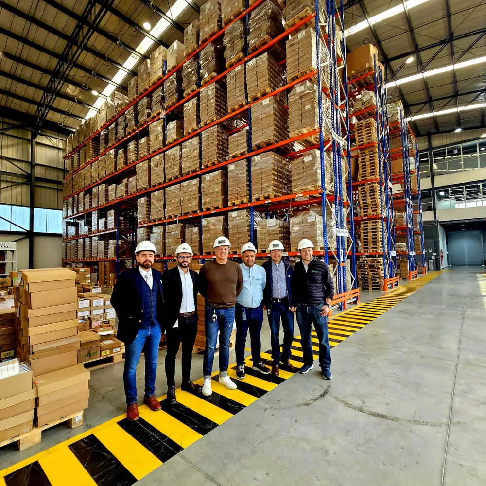 Heel Mitarbeiter stehen nebeneinander im neuen und modernen Distributionszentrum vor einem Hochregallager.