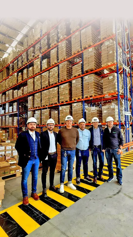 Heel Mitarbeiter stehen nebeneinander im neuen und modernen Distributionszentrum vor einem Hochregallager.