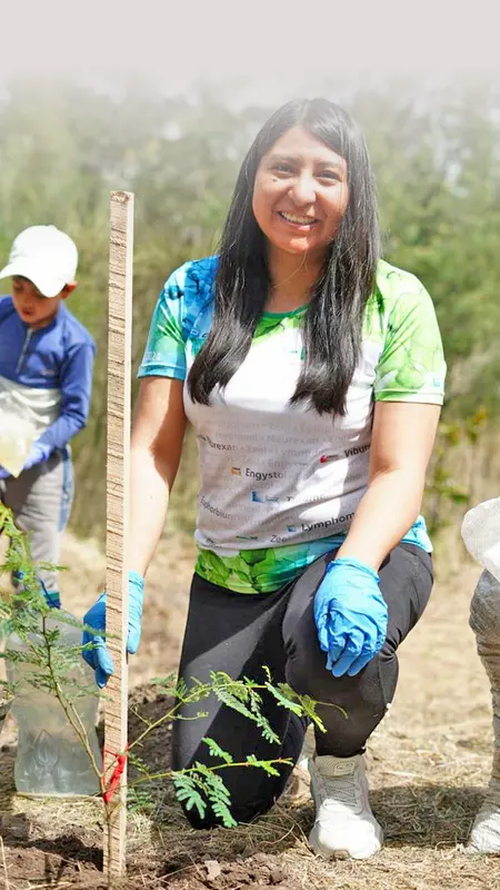 Heel Ecuador Mitarbeiterin pflanzt einen Baum mit Kind im Hintergrund