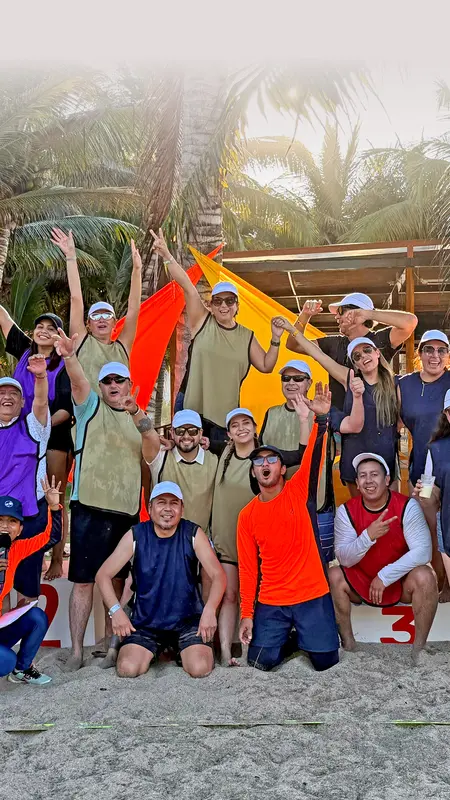 Heel Ecuador Mitarbeiter stehen als Gruppe am Strand und lachen in die Kamera. 