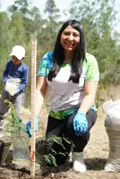 Heel Ecuador Mitarbeiterin pflanzt einen Baum mit Kind im Hintergrund