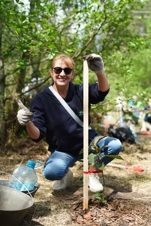 Heel Ecuador Mitarbeiterin präsentiert ihren frisch gepflanzten Baum und hält den Daumen hoch
