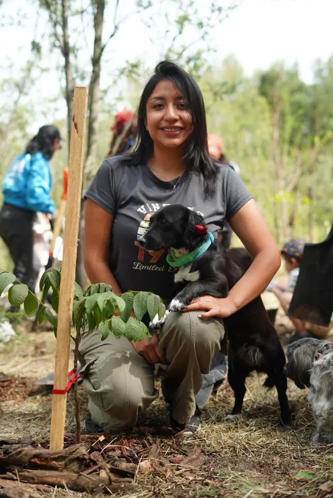 Heel Ecuador Mitarbeiterin vor ihrem gepflanzten Baum mit Hund auf Ihrem Schoß