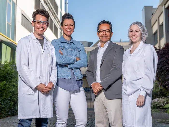 Mitarbeiter aus Labor, Produktion und kaufmännischen Bereich stehen vor dem Heel Gebäude und lächeln in die Kamera.