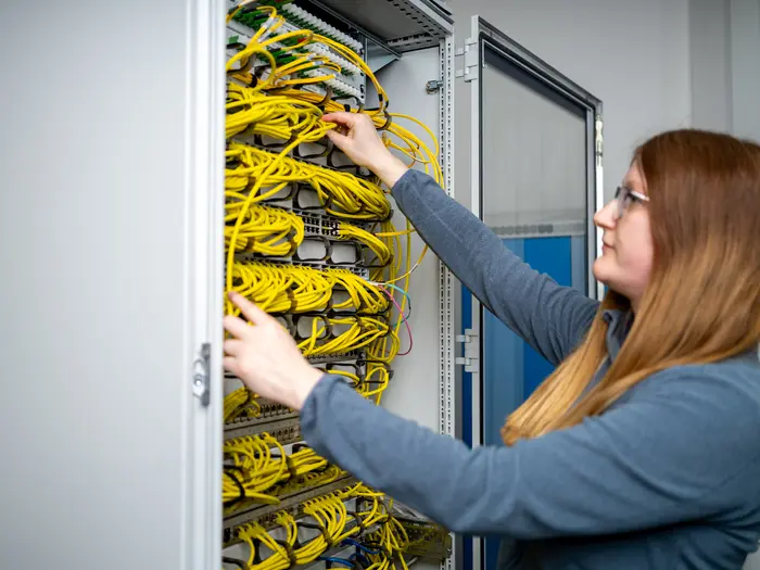 Eine IT-Mitarbeiterin steht vor einem Serverrack mit zahlreichen Netzwerkkabeln und schließt diese an.