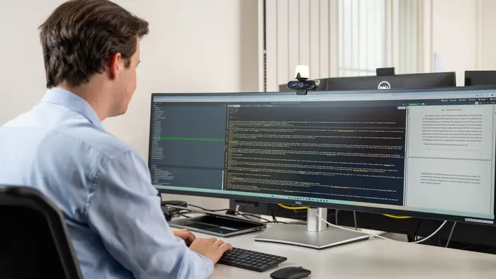 Ein Auszubildender Fachinformatiker für Daten & Prozessanalyse programmiert etwas an einen großen und modernen Bildschirm. 