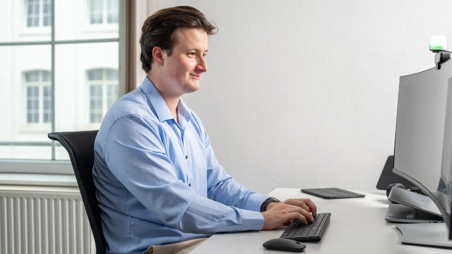 Ein Auszubildender Fachinformatiker für Daten & Prozessanalyse sitz an seinem Schreibtisch und schaut zufrieden in seinen PC-Bildschirm.