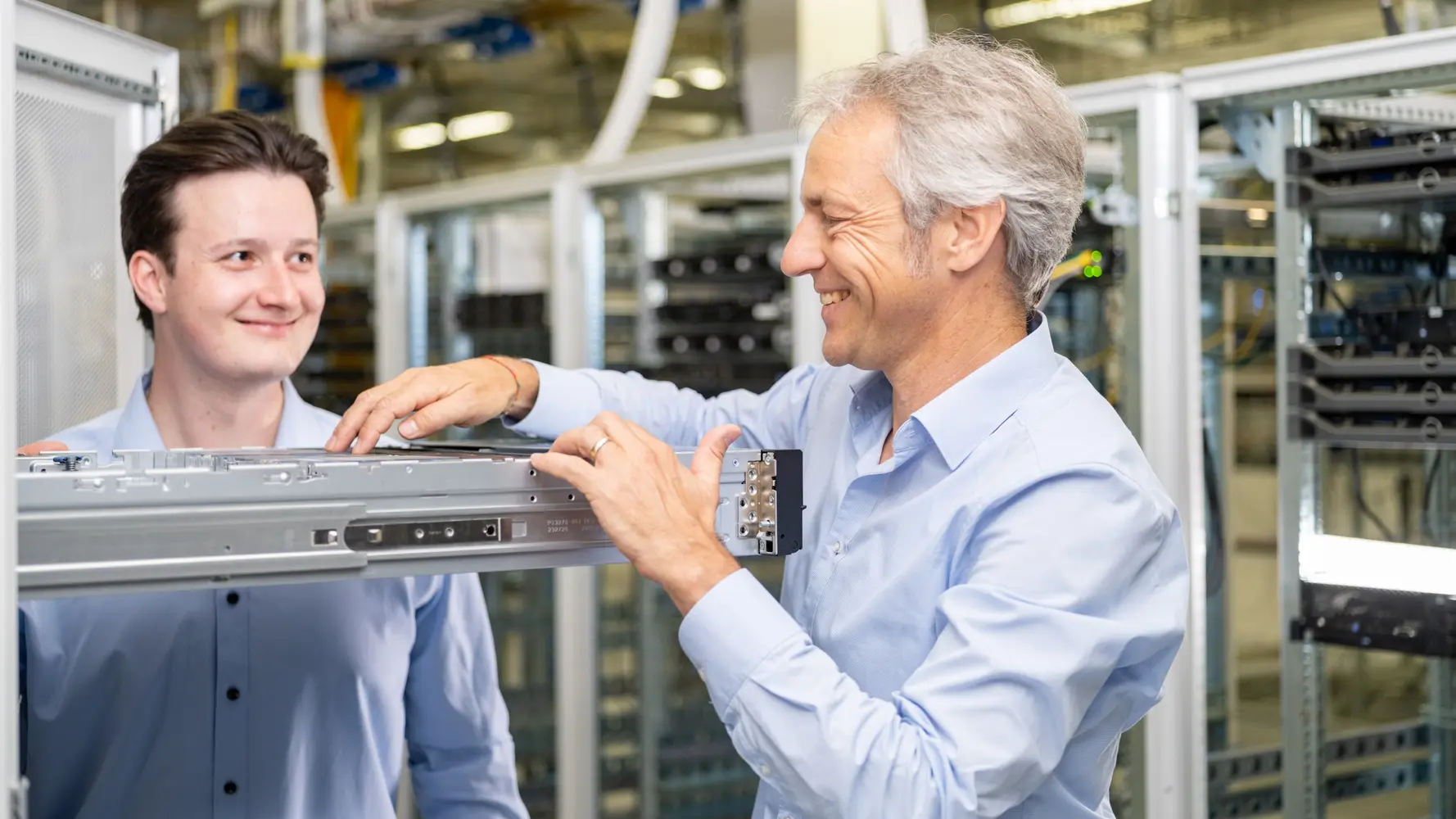 Ein Auszubildender Fachinformatiker für digitale Vernetzung und ein IT-Mitarbeiter stehen in einem Serverraum und inspizieren einen Server-Rack.