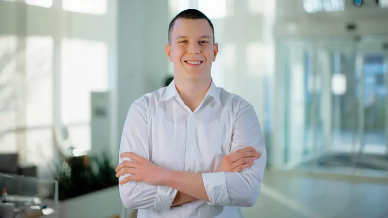 Ein dualer Wirtschaftsinformatikstudent lächelt mit verschränkten Armen in die Kamera.