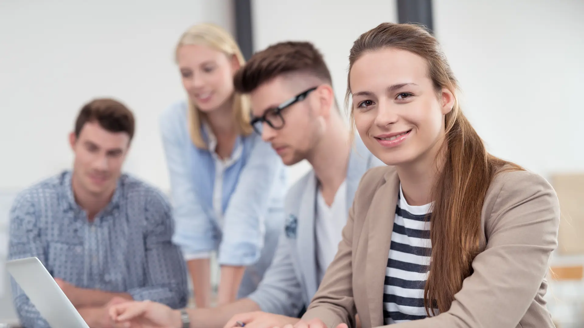Vier Studenten arbeiten gemeinsam an einem Laptop, eine Studentin lächelt in die Kamera. 