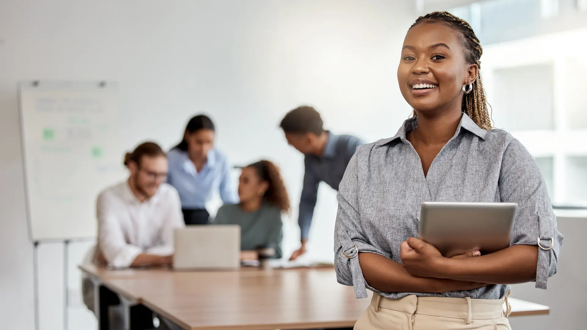 Lächelnde Masterstudentin steht vor einer Gruppe Studenten, die an einem Projekt arbeiten.