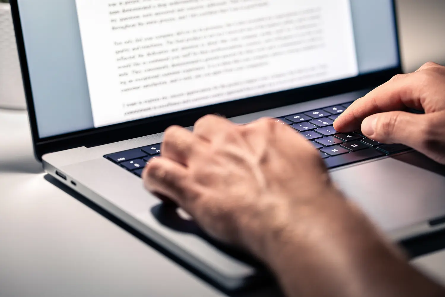Hände tippen einen Text in ein Dokument auf einem Laptop.