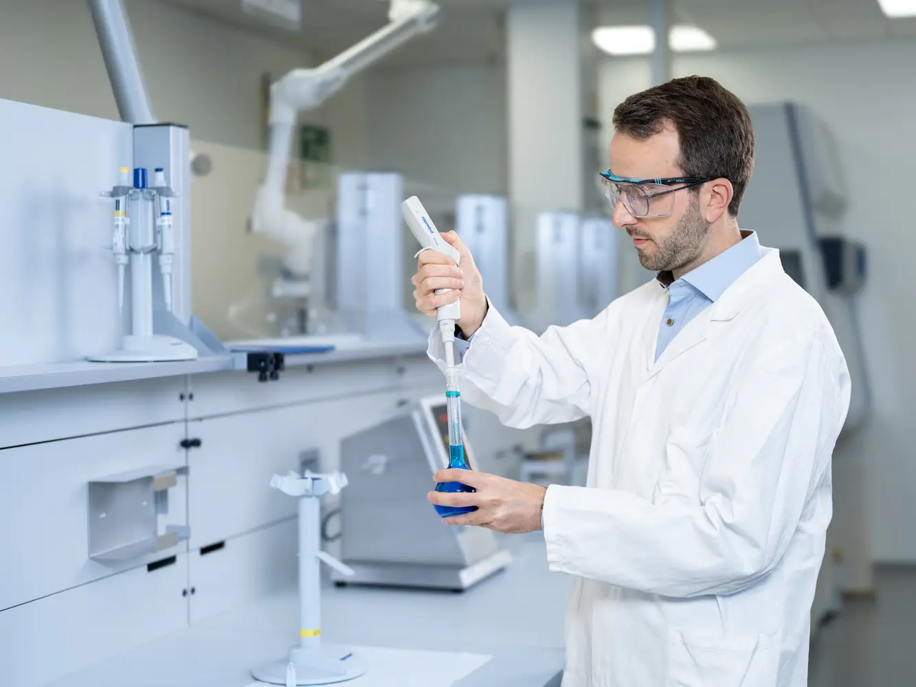 Chemielaborant füllt eine blaue Flüssigkeit mit Hilfe einer Labor-Mikropipette in einen konischen Kolben.