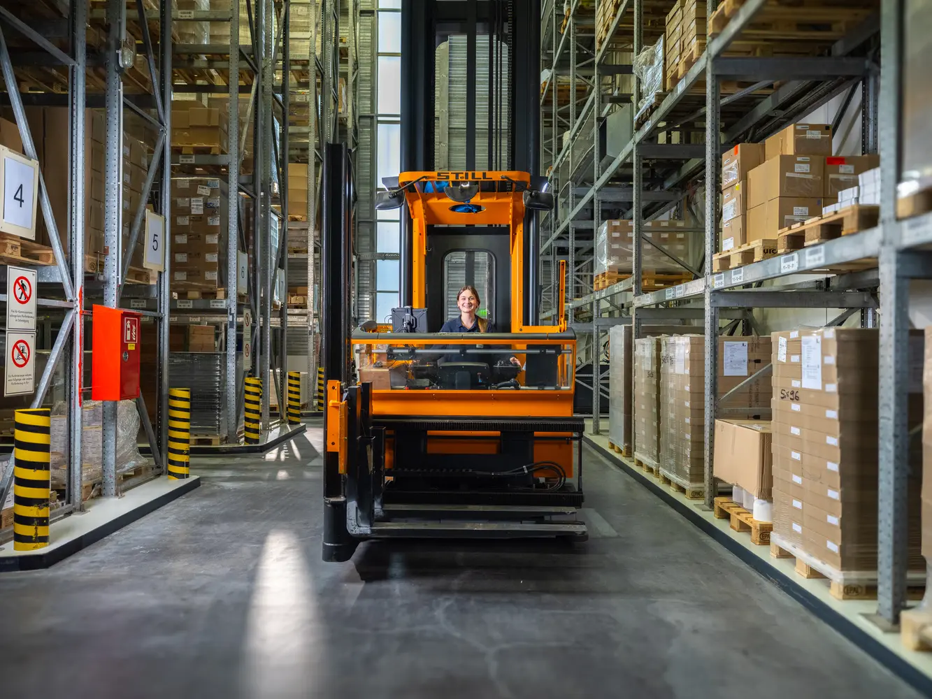 Logistikmitarbeiterin fährt einen Gabelstapler durch das Lager.